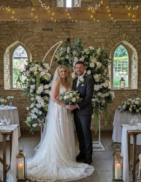 Broken Arch - "Grace" Bride and groom smiling together in a decorated venue surrounded by flowers.